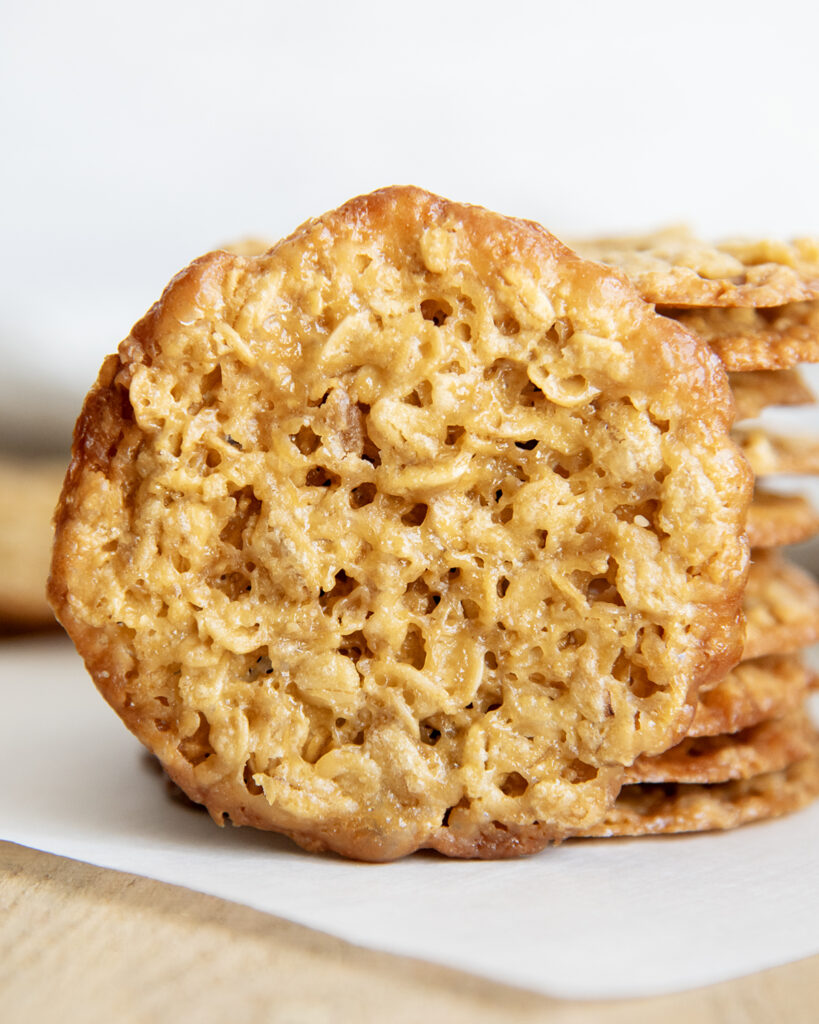 A golden colored oatmeal lace cookie set up against a stack of cookies.