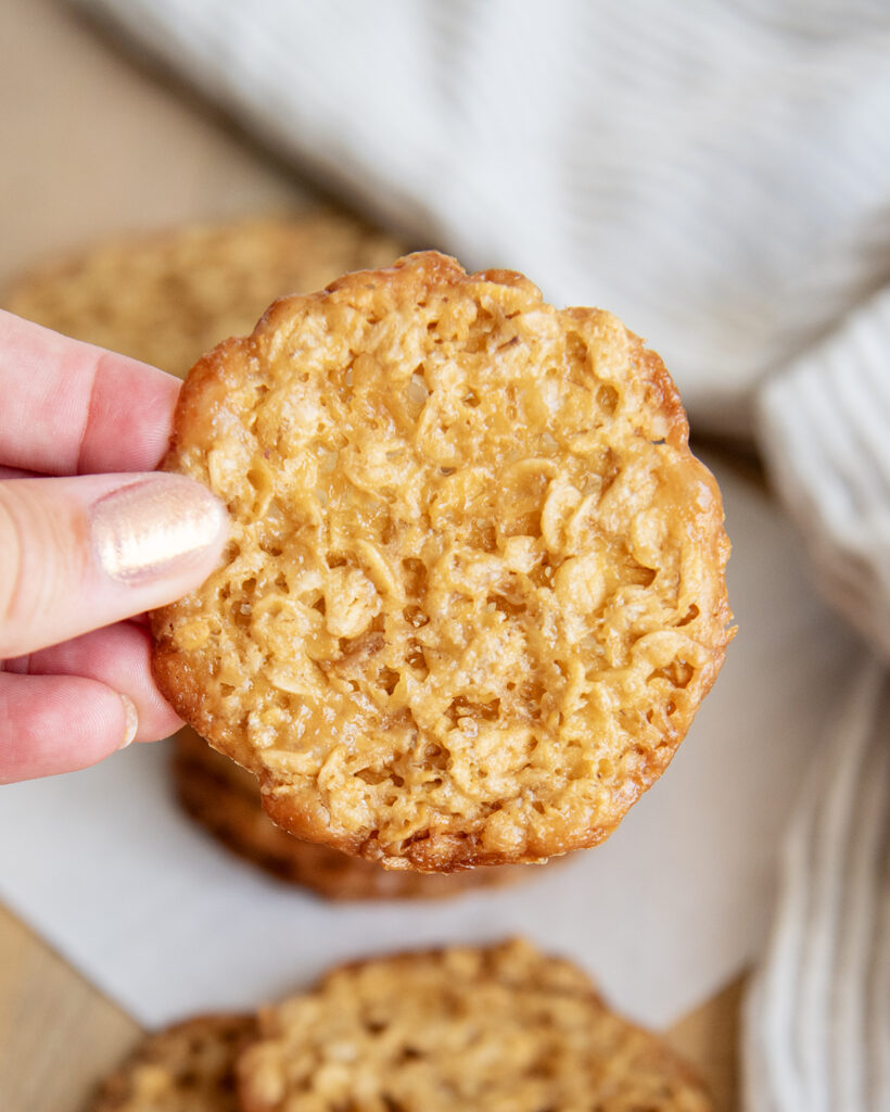 A hand holding a thin oatmeal lace cookie.