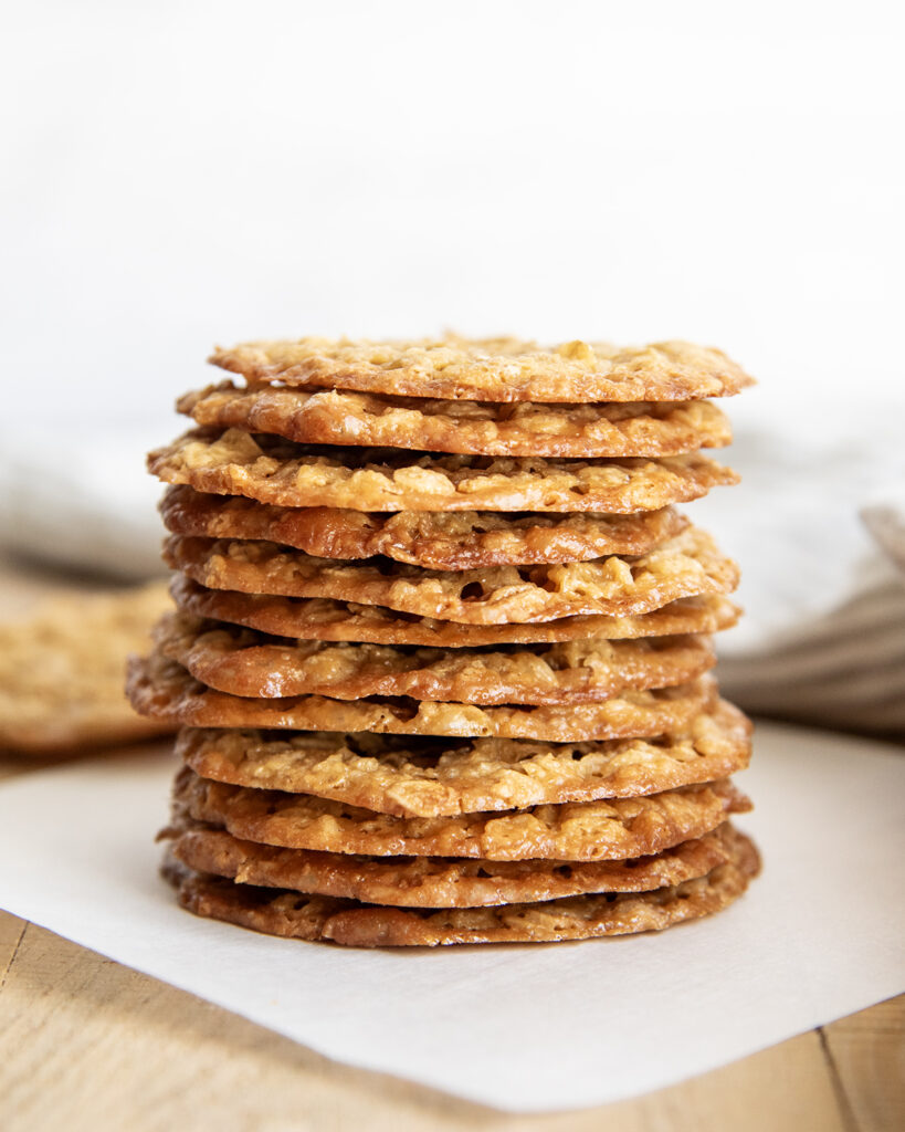 A stack of golden colored oatmeal lace cookies on a piece of parchment paper.