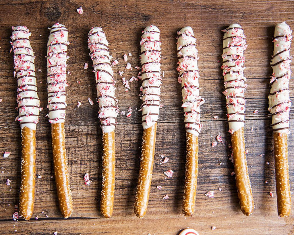 A row of pretzel rods dipped in white chocolate, and topped with peppermint pieces.