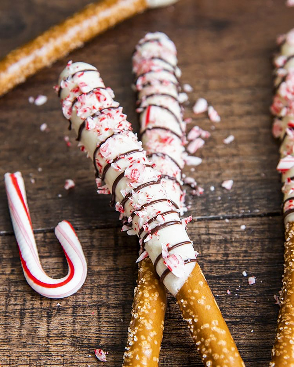 Two pretzel rods dipped in white chocolate and drizzled with chocolate, and topped with peppermint candy cane pieces.