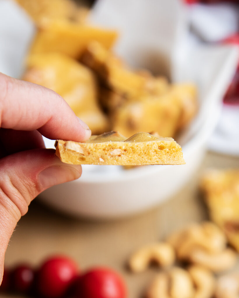 A hand holding a piece of cashew brittle.