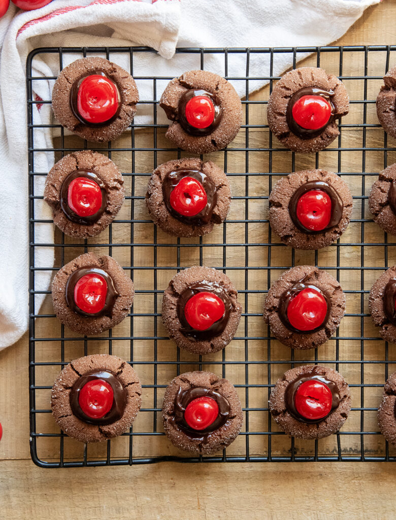 An above view of chocolate cherry thumbprint cookies on a wire cooling rack.