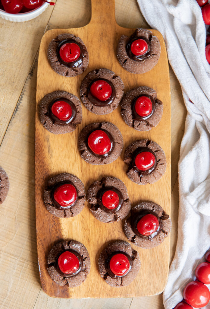 An above view of chocolate cherry thumbprint cookies on a small wooden board.