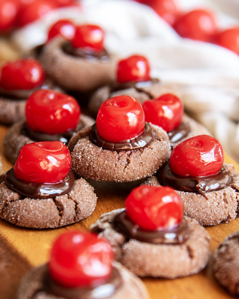 A pile of chocolate cherry cookies topped with chocolate ganache and red maraschino cherries. 