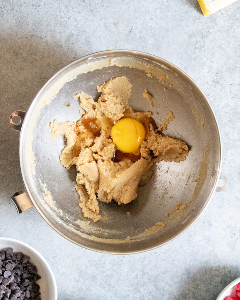 A bowl of creamed butter and sugar topped with an egg, and vanilla extract.