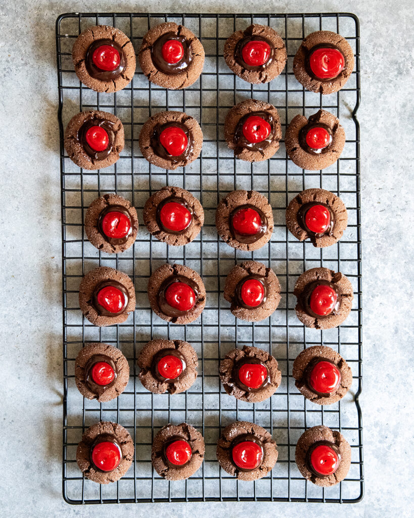 An above view of chocolate cherry thumbprint cookies on a wire cooling rack.