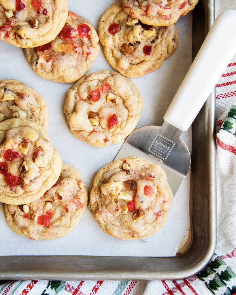 A fruitcake cookie on a metal spatula on a cookie sheet.