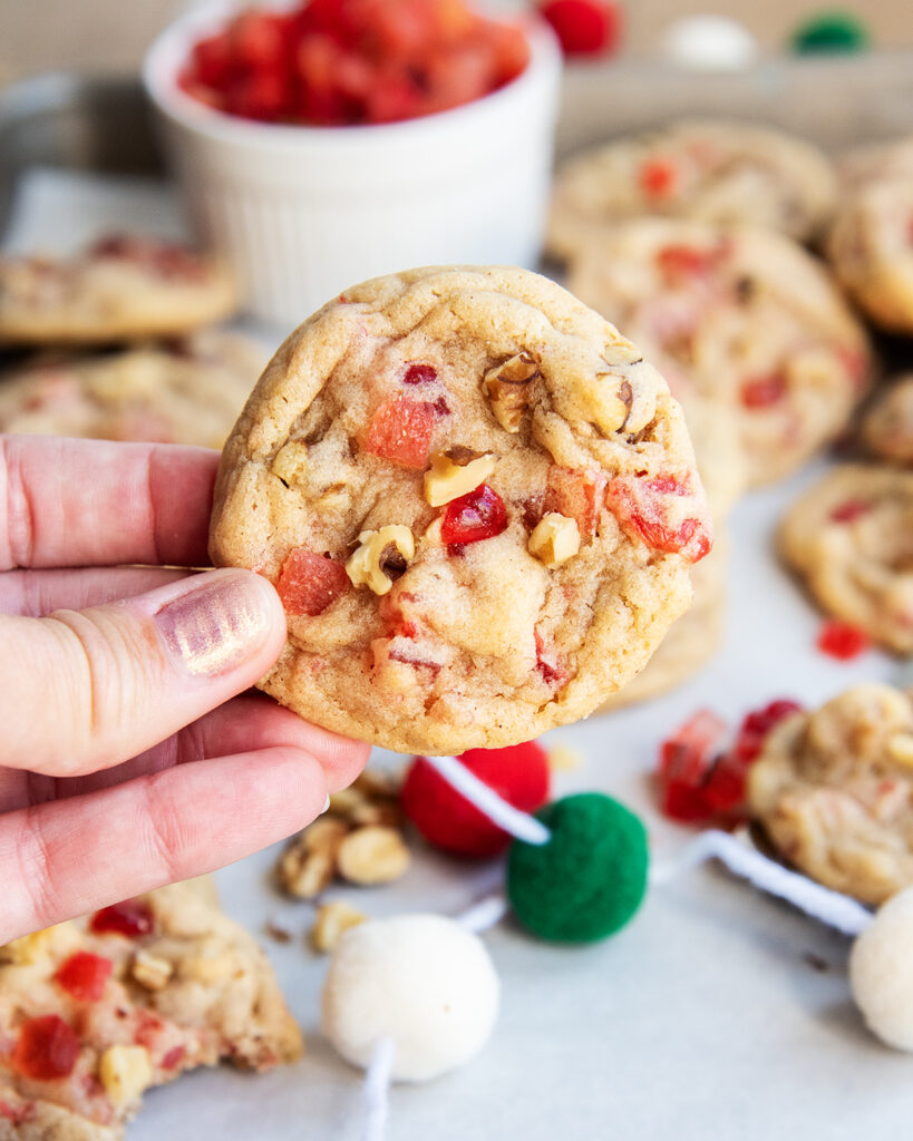 A hand holding a fruitcake cookies full of dried fruit pieces and walnuts.