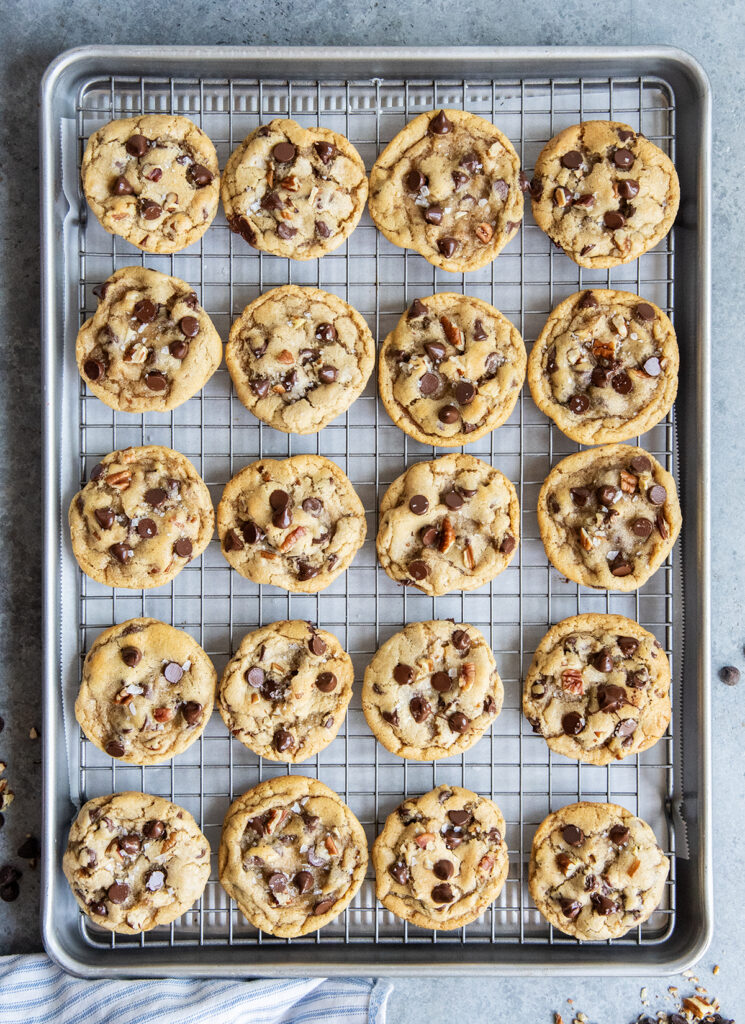 A wire rack topped with rows of pecan and chocolate chip cookies topped with flaky sea salt.