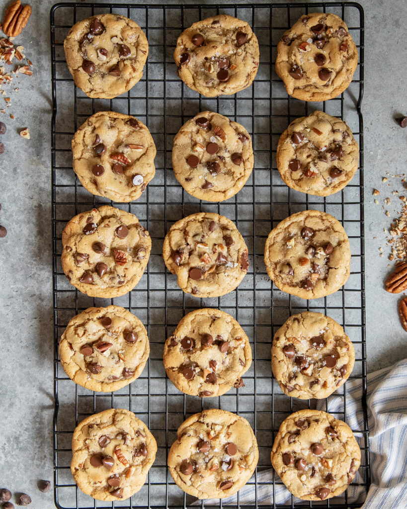 A wire rack topped with rows of pecan and chocolate chip cookies topped with flaky sea salt.