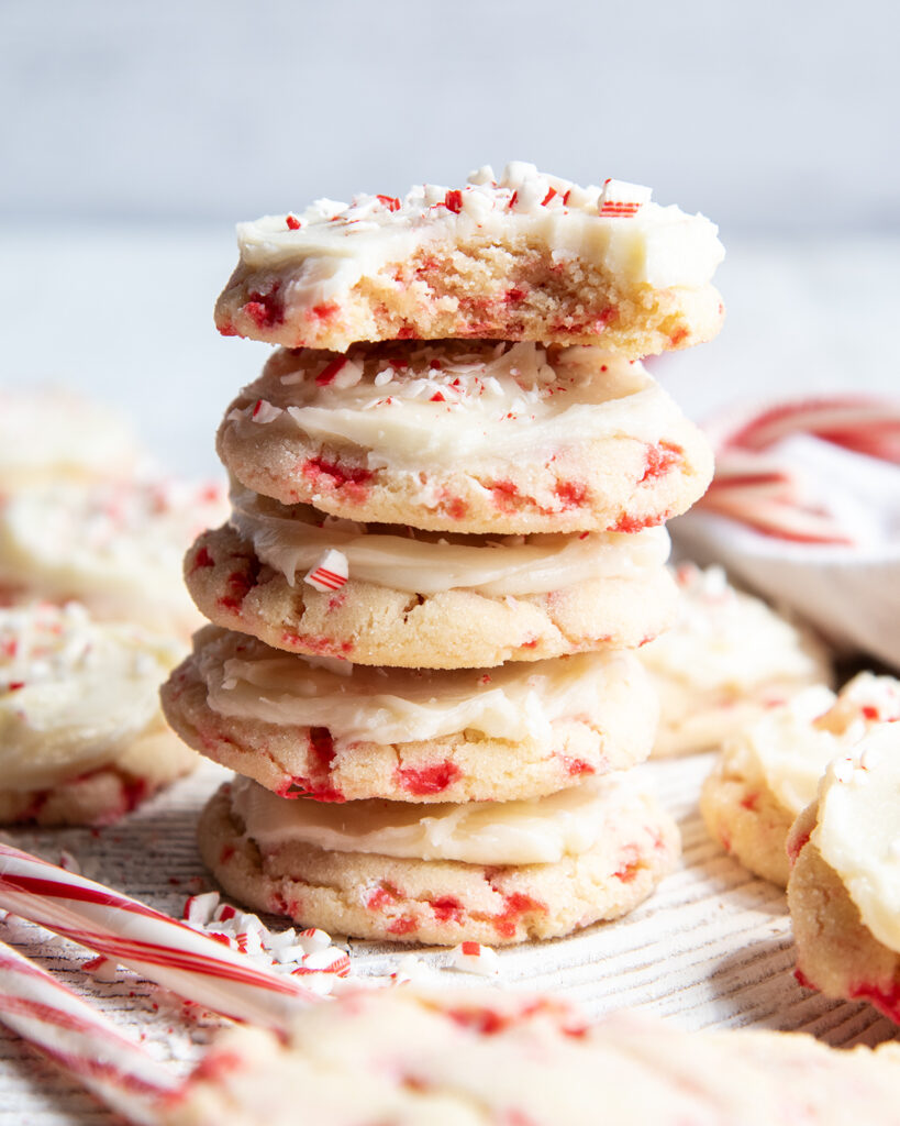 A stack of 5 peppermint frosted sugar cookies, and the top cookie has a bite out of it. 