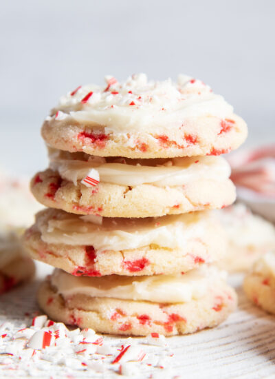 A stack of 4 Candy Cane Cookies with frosting, and candy cane pieces.