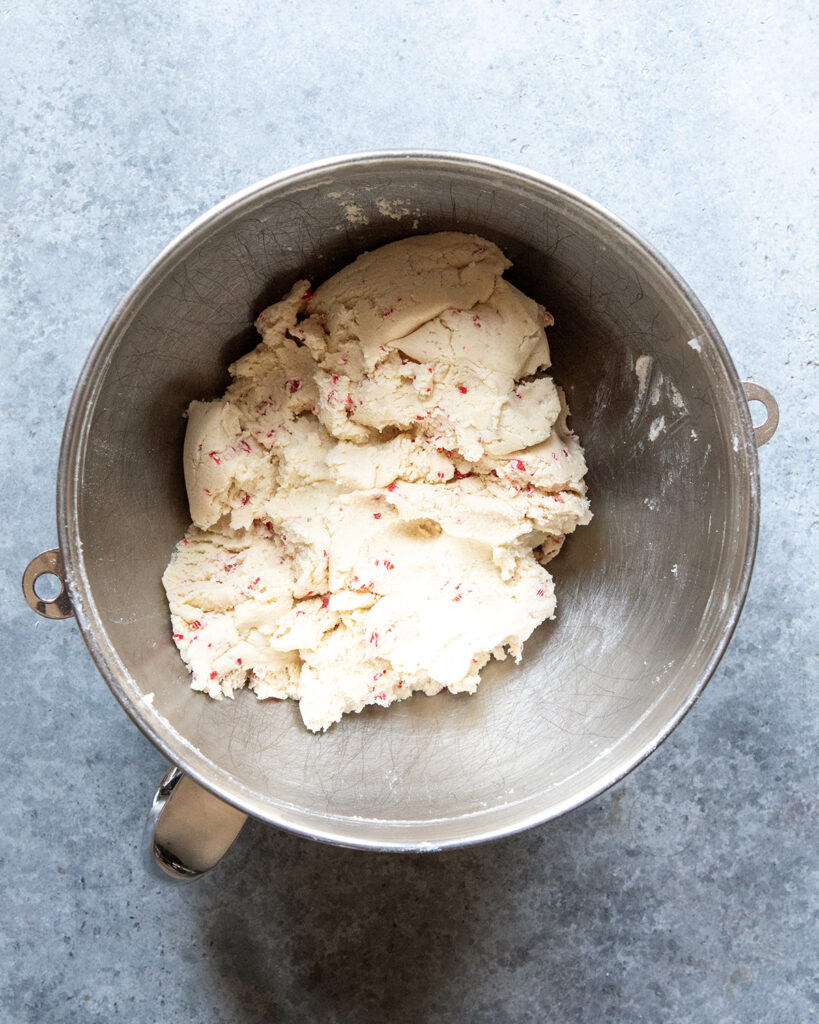 A bowl of a light colored cookie dough with candy cane pieces in it. 