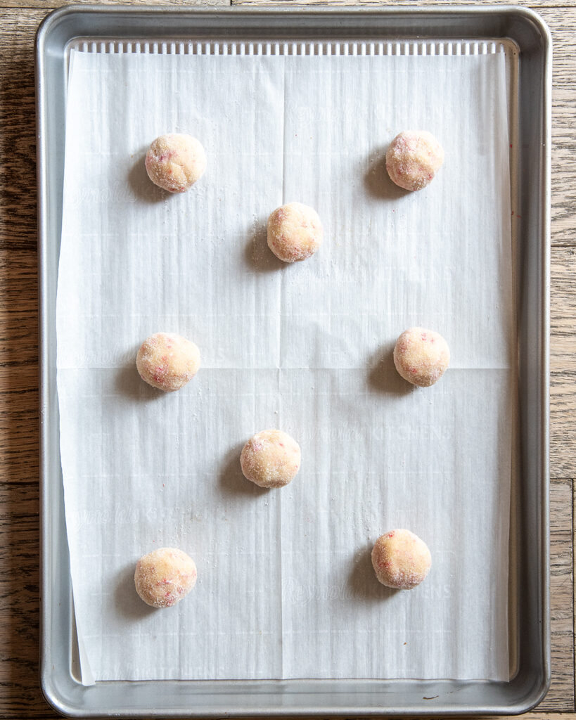 Balls of cookie dough rolled in granulated sugar on a cookie sheet.