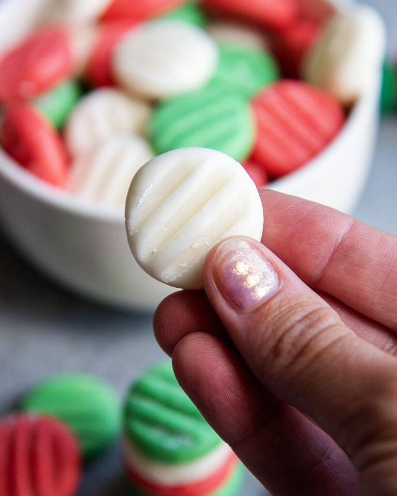 A hand holding a white cream cheese mint, with fork indents on the top.