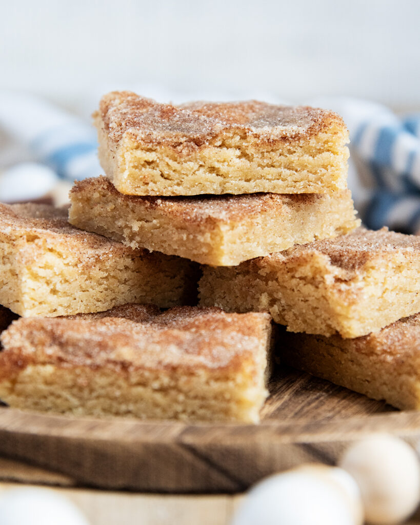 A pile of cookie bars on a wooden plate, topped with a cinnamon sugar crust.