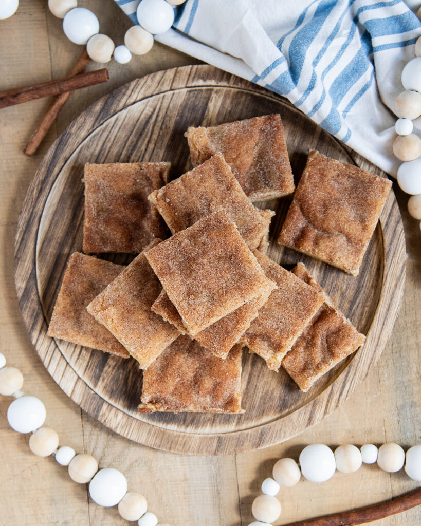 An above view of a pile of cookie bars on a wooden plate, topped with a cinnamon sugar crust.