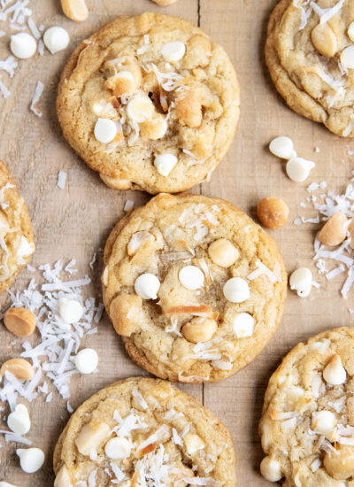 An above view of cookies topped with macadamia nuts, white chocolate chips, and coconut pieces.