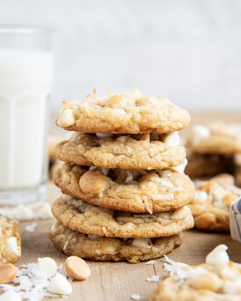 A stack of 5 white chocolate Coconut Macadamia Nut Cookies next to a glass of milk.