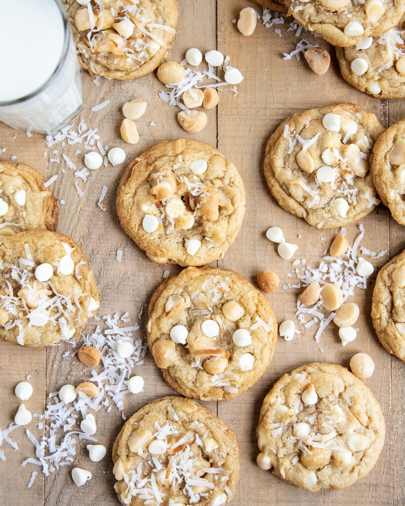 An above view of cookies topped with macadamia nuts, white chocolate chips, and coconut pieces.