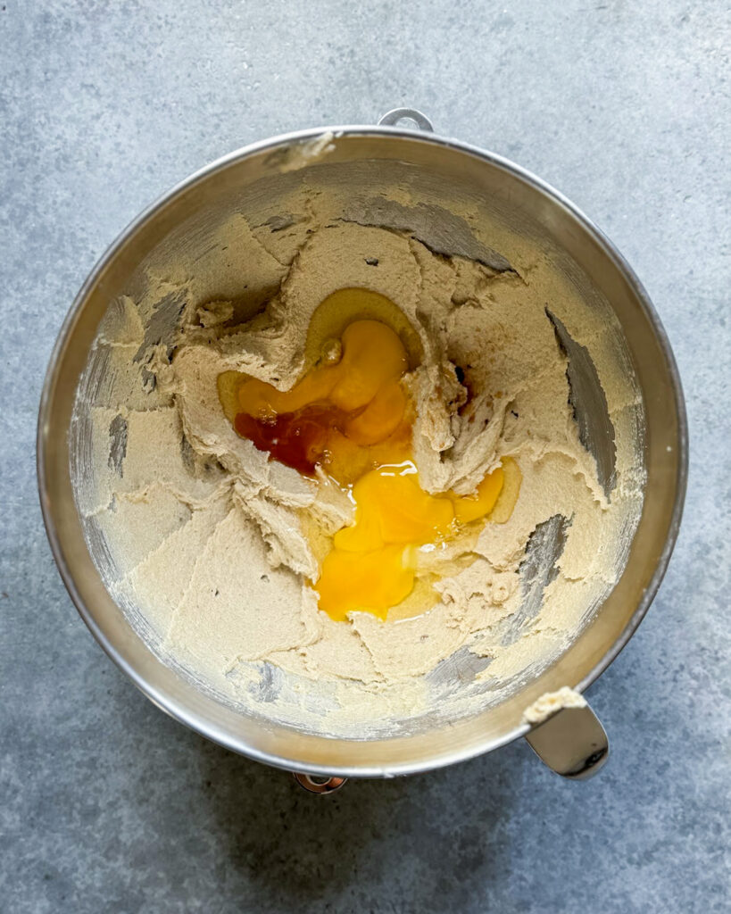 A bowl of creamed butter and sugar topped with an egg, and vanilla extract. 