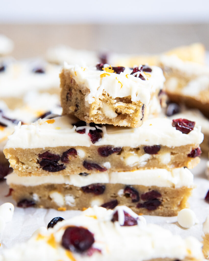 A stack of three white chocolate cranberry cookie bars, and the top bar has a bite out of it.