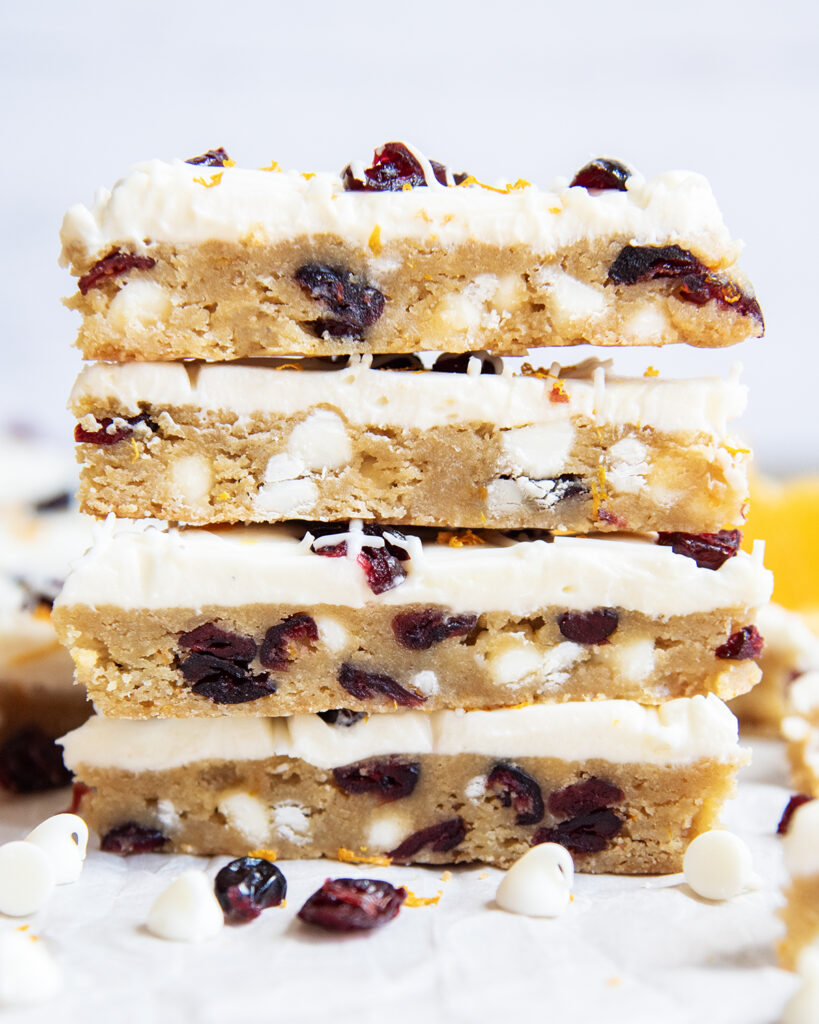 A stack of 4 White Chocolate Cranberry Bars with cream cheese frosting on top.