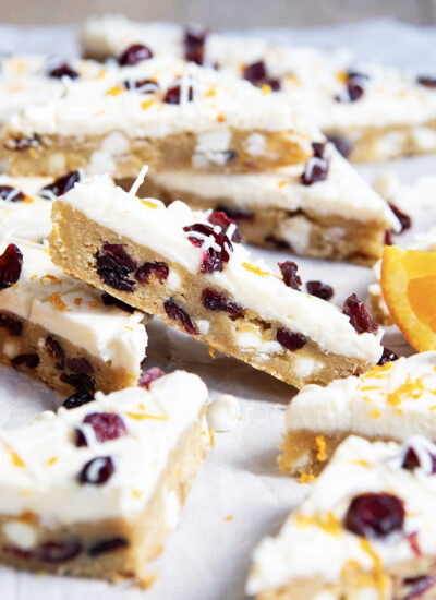 A White Chocolate Cranberry Bar leaning on another bar with cream cheese frosting on top.