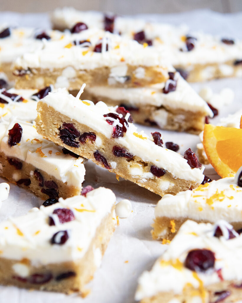 A White Chocolate Cranberry Bar leaning on another bar with cream cheese frosting on top. 