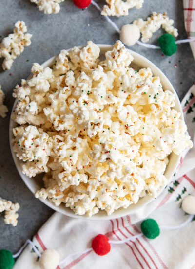 An above view of a bowl of white chocolate coated popcorn, topped with tiny round sprinkles.