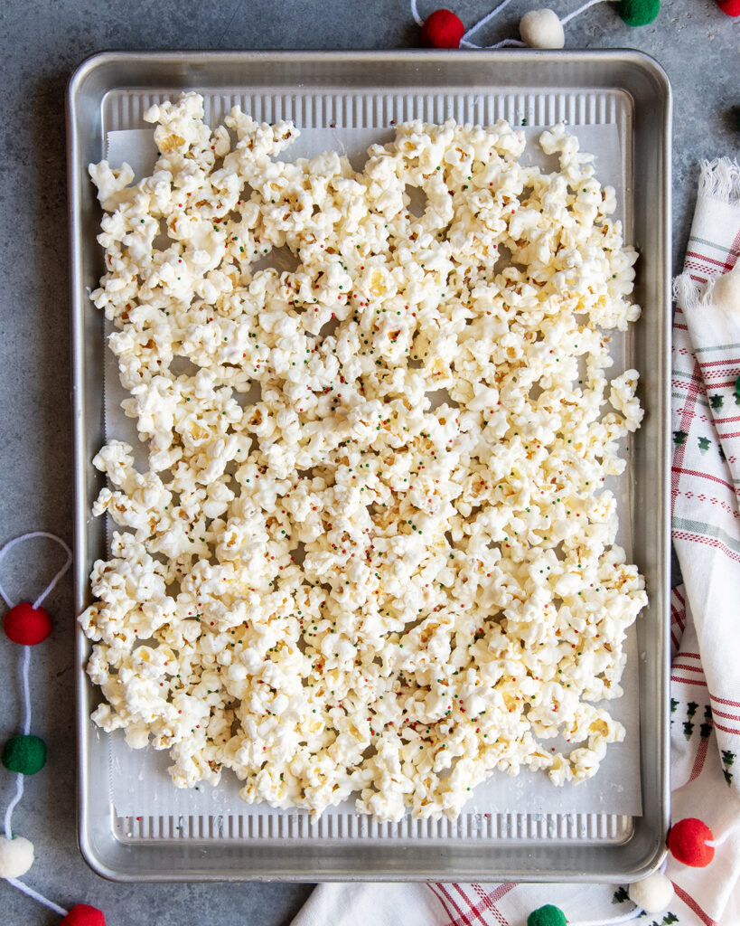 A baking pan topped with white chocolate coated popcorn, topped with non pareil sprinkles.