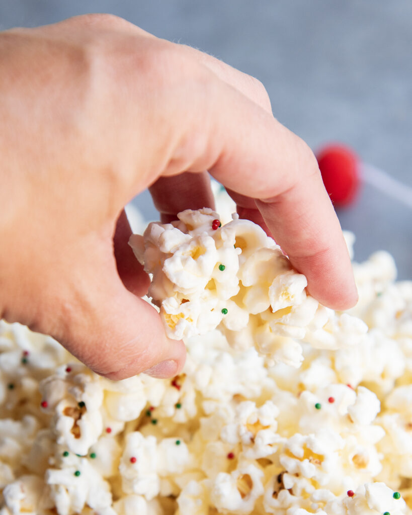 A hand grabbing a piece of white chocolate popcorn out of a bowl.