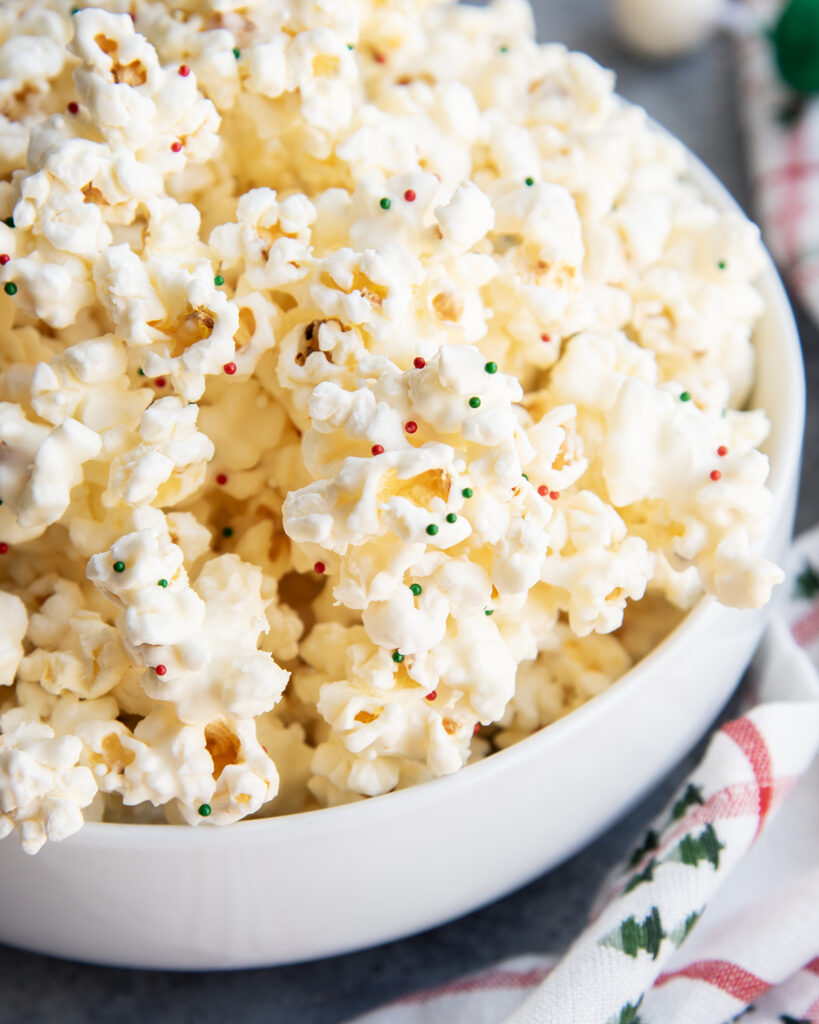 A bowl of white chocolate popcorn topped with red, green, and white sprinkles.