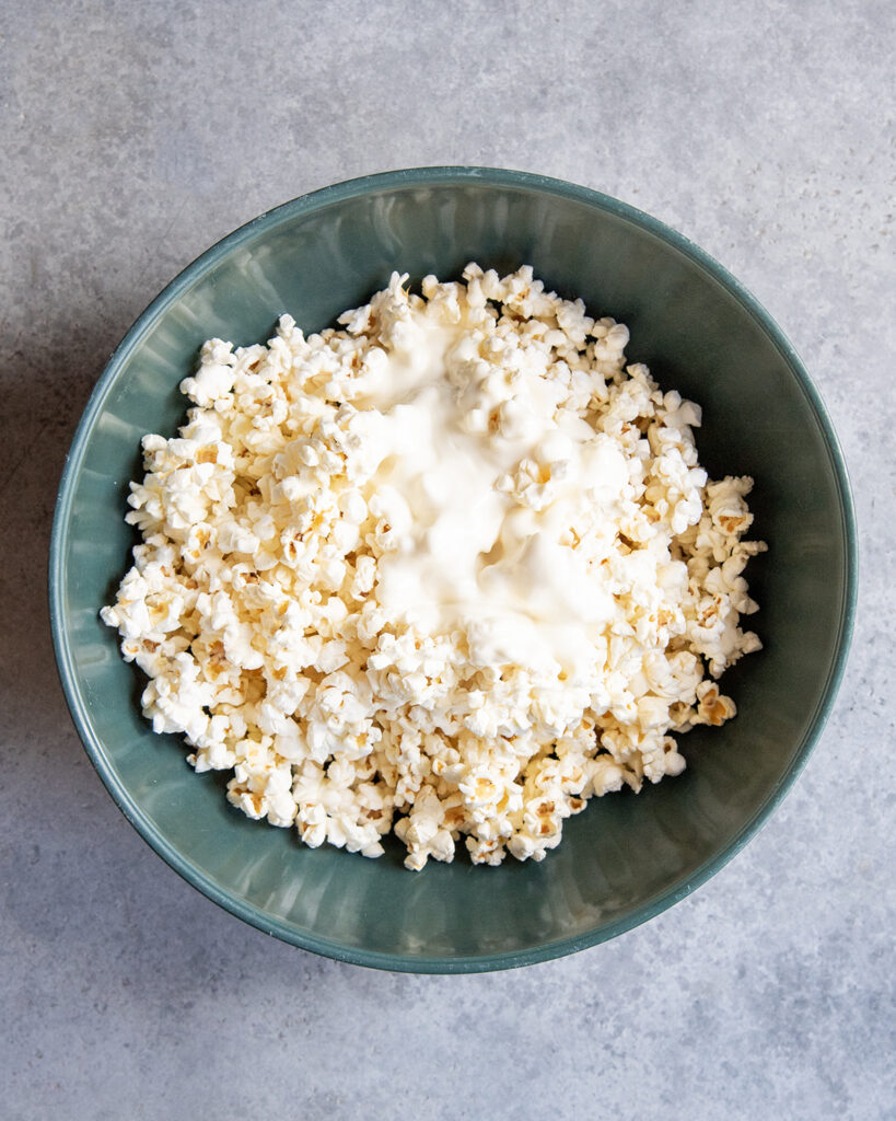 A bowl of popcorn with melted white chocolate on top.