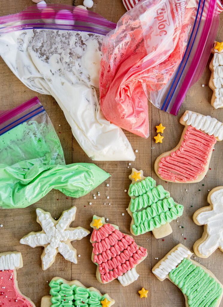 Three bags of buttercream frosting for sugar cookies, next to frosted sugar cookies.