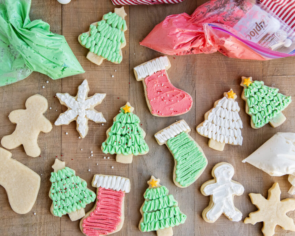 Three bags of buttercream frosting for sugar cookies, next to frosted sugar cookies.