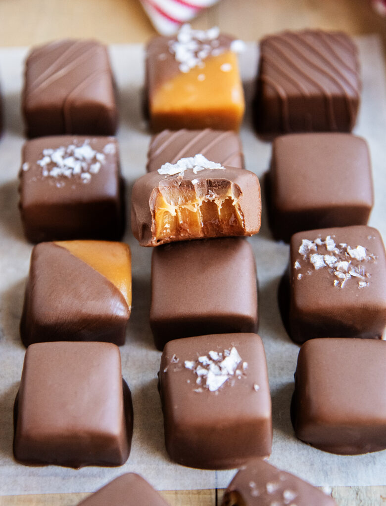 Chocolate covered caramels on a piece of parchment paper. One on top has a bite out of it.