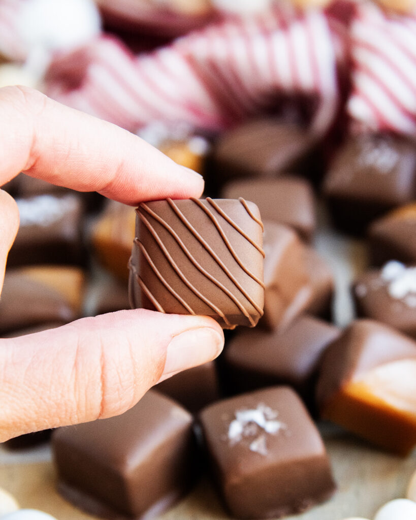 A hand holding a chocolate coated caramel candy, with drizzles across the top.