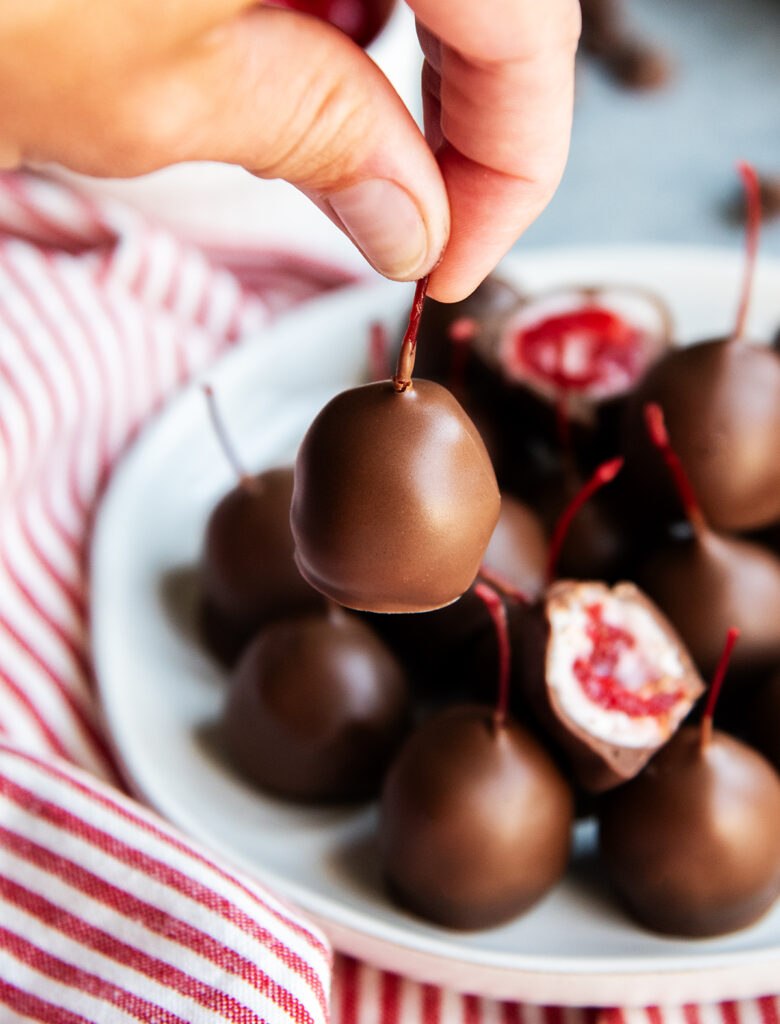 A hand holding a chocolate covered cherry by the stem. 