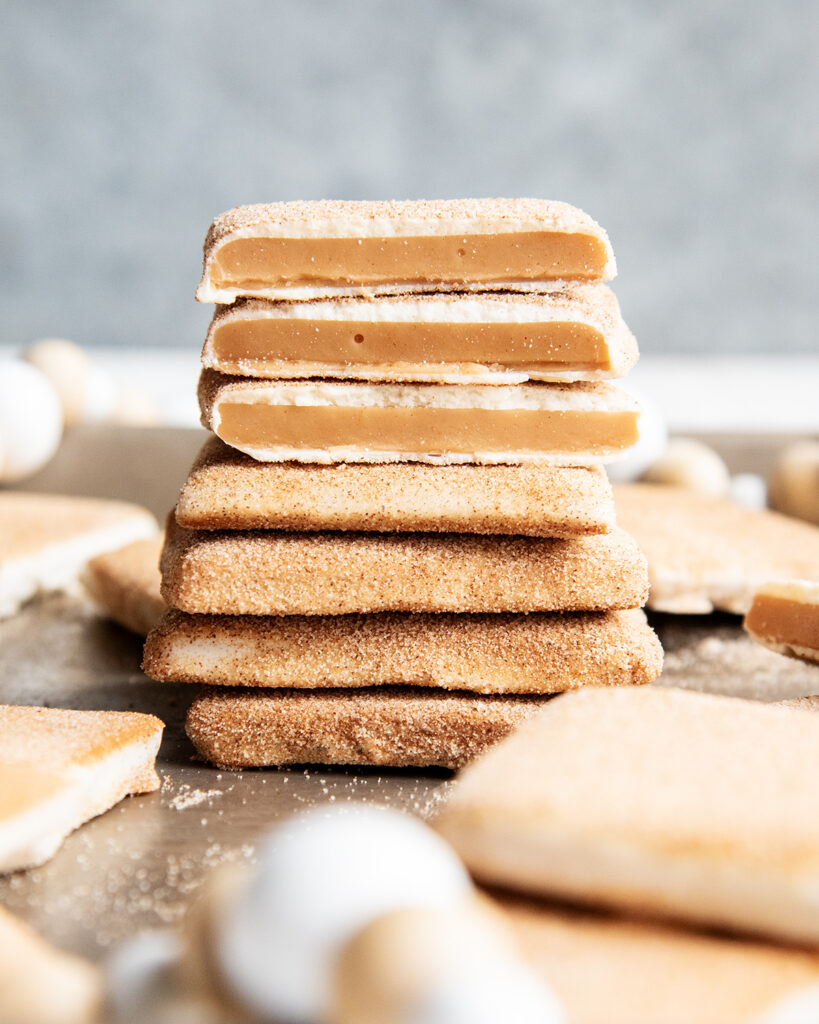 A stack of cinnamon sugar and white chocolate churro toffee. The top three pieces are broken in half showing the middle of the toffee.