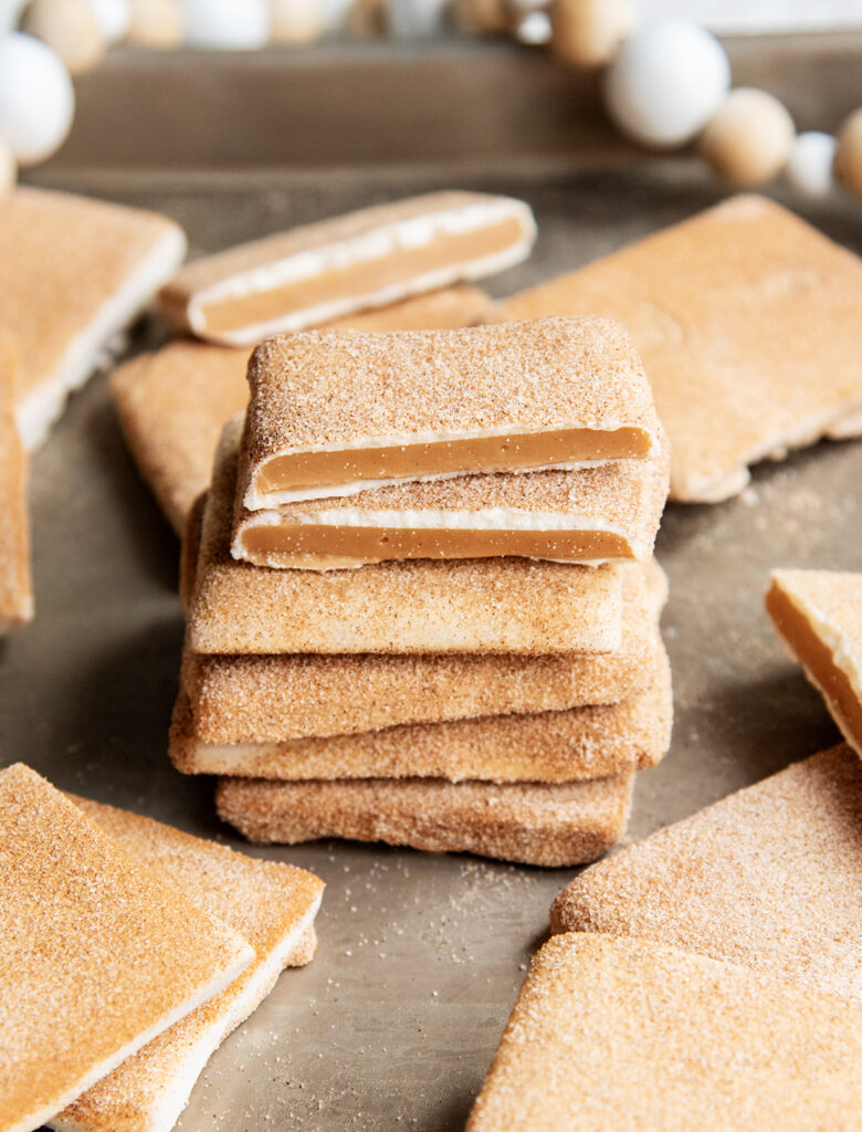 A stack of pieces of cinnamon sugar coated toffee showing the toffee in the middle of white chocolate.