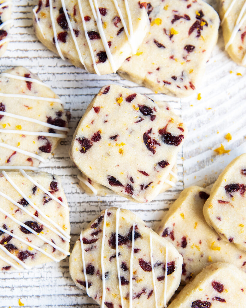 Cranberry Orange Shortbread on a white table, some of the cookies are drizzled with lines of white chocolate.