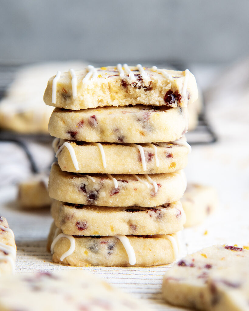 A stack of small cranberry orange shortbread cookies. The top cookie has a bite out of it.