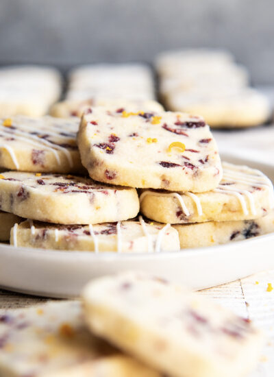 A plate of cranberry orange shortbread cookies that are drizzled with white chocolate.