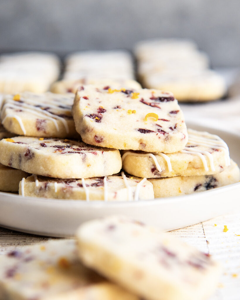 A plate of cranberry orange shortbread cookies that are drizzled with white chocolate.