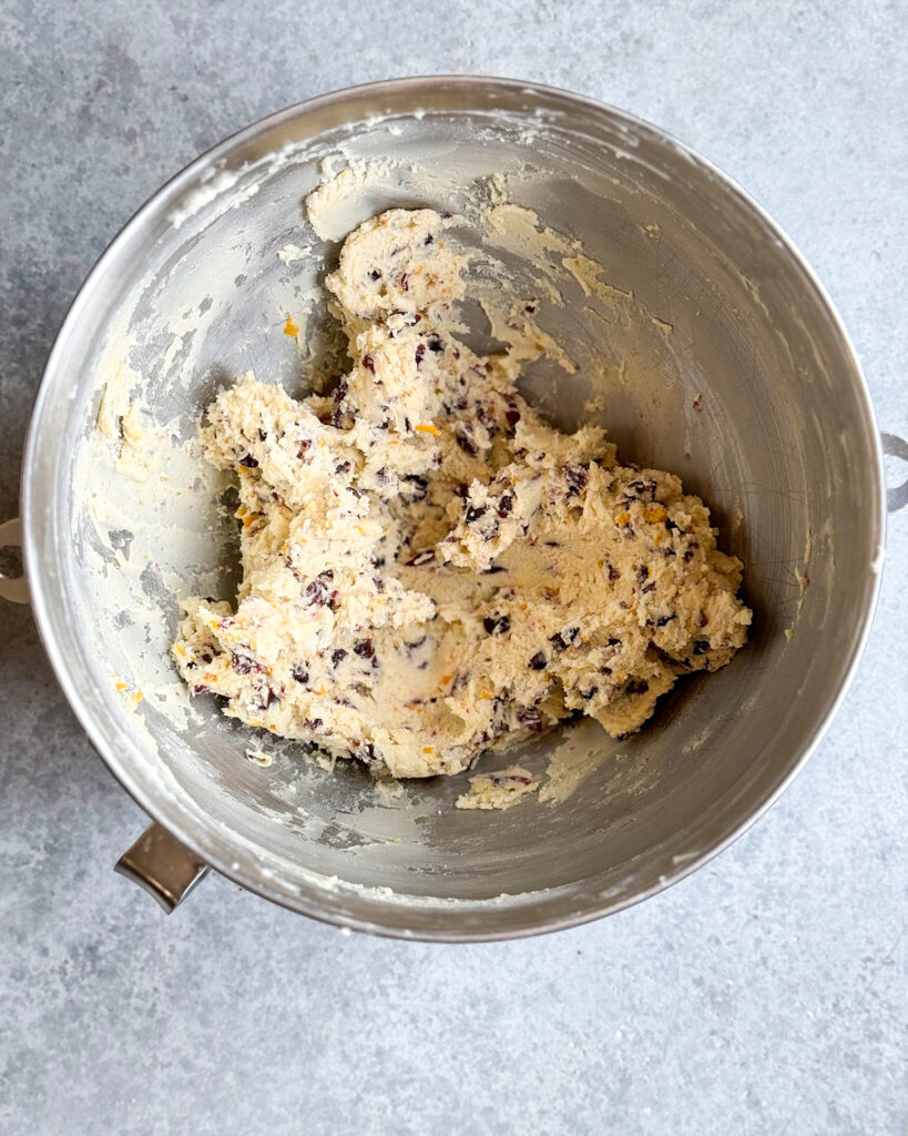 A metal bowl full of cookie dough that is loaded with chopped up dried cranberry pieces.