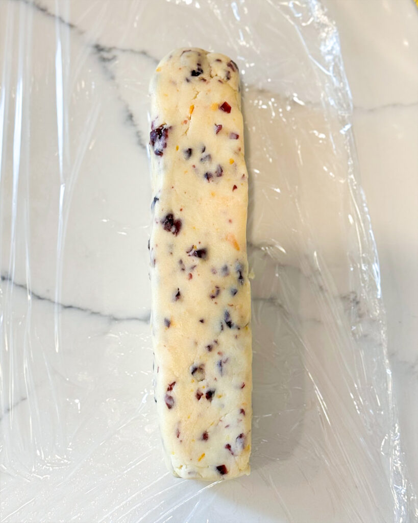 A squared off log of shortbread cookie dough laying on plastic wrap. 