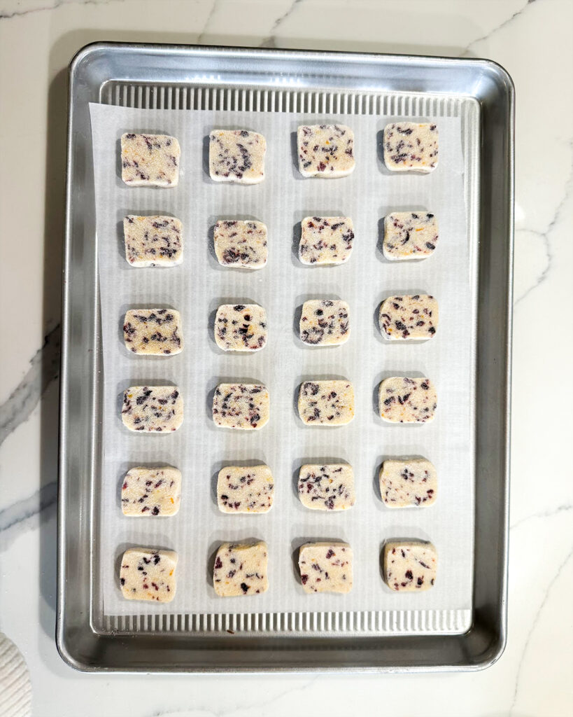 Square cranberry shortbread cookie dough pieces on a metal baking sheet.