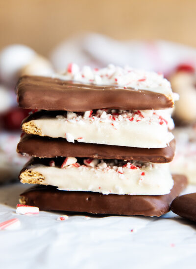 A stack of Peppermint Bark Graham Crackers that are dipped half in chocolate, half in white chocolate, and topped with peppermint candies.